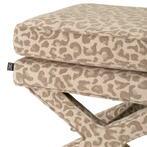 Taburete otomano de tela estampada en color beige con asiento acolchado y base en forma de cruz - Mobiliario de lujo para hoteles Vista detalle por Luxury Group International