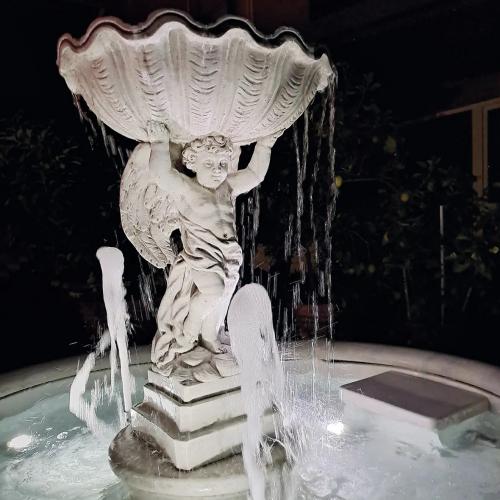 Fontaine d'eau baroque de luxe avec chérubin et vasque supérieure sculptée dans un bassin incurvé - Fontaine baroque Vue de côté par Luxury Group International