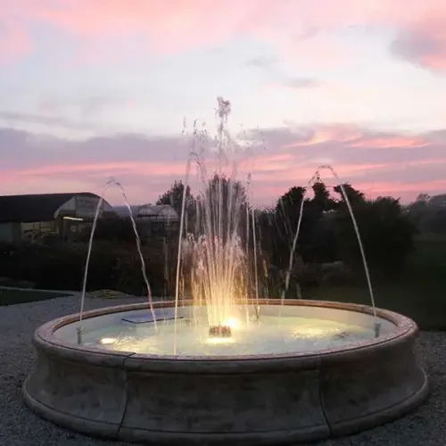 Luxus Barockbrunnen mit Steinoptik, beleuchtetem Mittelstrahl & radialen Bogenfontänen – Barockbrunnen Lifestyle-Ansicht von Luxury Group International
