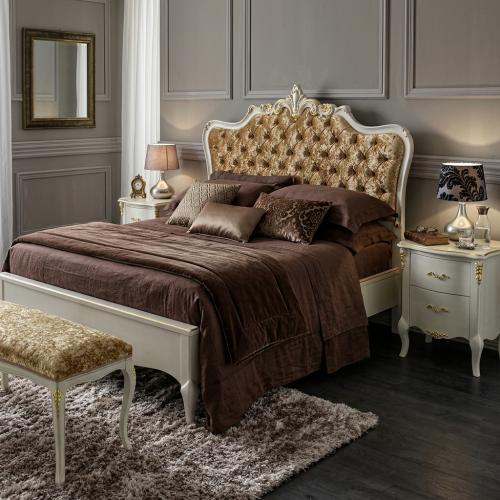 Weißes Barock-Luxusbett mit goldgepolstertem, geknöpftem Kopfteil und skulptiertem Kronenwappen – Barockmöbel Lifestyle-Ansicht von Luxury Group International